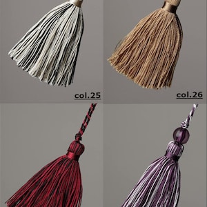 May include: Four different coloured tassels with a decorative bead at the top. The tassels are black and white, brown, red and black, and purple and white.