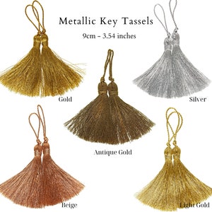 Op de afbeelding: Vijf metalen sleutelkwastjes in verschillende kleuren: goud, antiekgoud, lichtgoud, beige en zilver. Elk kwastje is 9 cm of 3,54 inch lang.