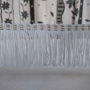 May include: White fringe trim with a gold thread running through it. The fringe is approximately 2.5 cm long.