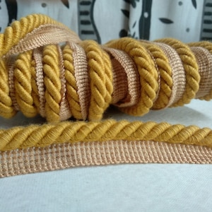 May include: A close-up of a spool of yellow and beige rope trim. The rope is twisted and has a textured surface.