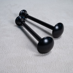 Könnte beinhalten: Zwei schwarze Metall-Gardinenstangen mit runden Endkappen. Die Stangen liegen auf einer weißen Oberfläche.