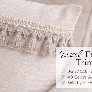 Puede incluir: Primer plano de un cojín beige con un ribete decorativo de flecos y borlas. El ribete mide 3 cm de ancho y presenta pequeñas borlas. La imagen incluye el texto "Tassel Fringe Trim".