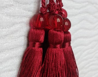 May include: Three red tassels with red glass beads at the top. The tassels are made of a soft, silky material.
