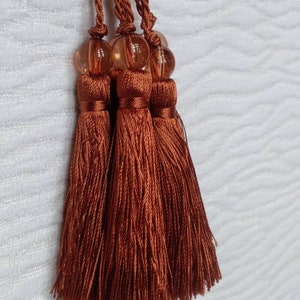 Peut inclure: Quatre glands de couleur marron avec des perles de verre ambrées en haut. Les glands sont faits d'un matériau doux et soyeux.
