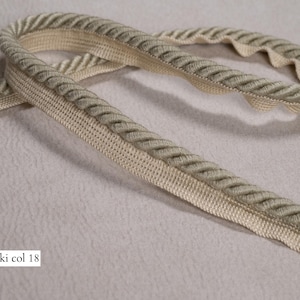 May include: A close-up of a beige and khaki rope trim. The trim has a braided design and a scalloped edge. The text "Khaki col 18" is visible in the image.
