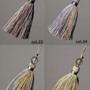 May include: Four tassel ornaments with a decorative bead at the top. The tassels are in four different colour combinations: purple and white, blue and yellow, yellow and blue, and green and brown.