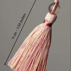 May include: A pink and cream tassel with a clear bead and a loop. The tassel is 9 cm or 3.54 inches long. The loop is 4 cm or 1.57 inches long. col.37