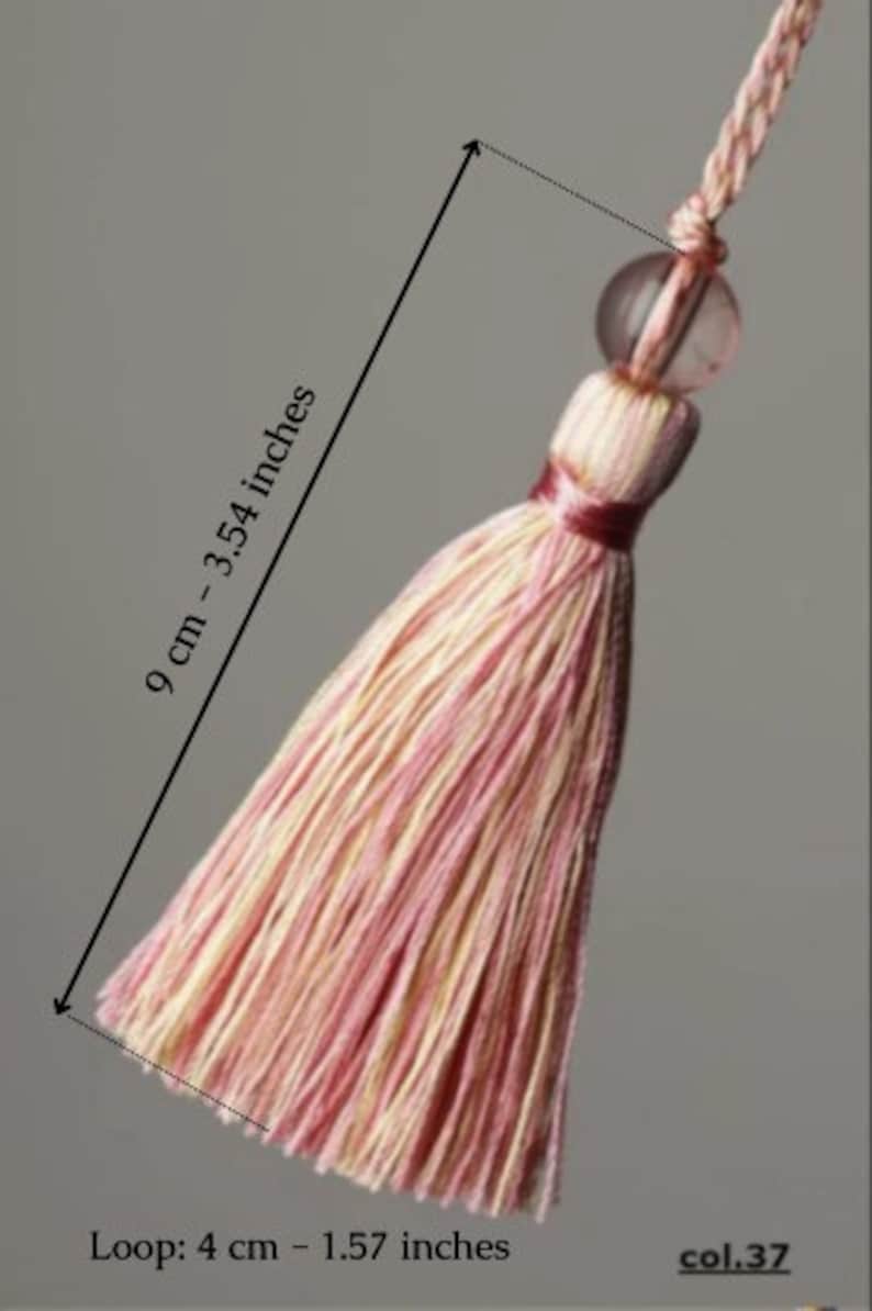 May include: A pink and cream tassel with a clear bead and a loop. The tassel is 9 cm or 3.54 inches long. The loop is 4 cm or 1.57 inches long. col.37