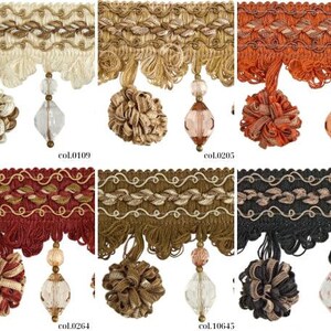 May include: Close-up of decorative trim samples in various colors. Each trim features a wavy top edge, a tassel, and a beaded pendant. Colors include cream, gold, orange, burgundy, olive green, and black. The product codes are visible.