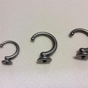May include: Three silver metal hooks of different sizes. The hooks are curved and have a round base.