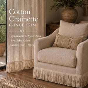 Op de afbeelding: Cotton Chainette FRINGE TRIM. Continuous 10 Meter Piece. 4 Available Colors. Length: 10cm – 60cm. Een beige gordijn en een beige fauteuil, beide voorzien van lange, hangende franje langs de onderranden, met een beige kussen met textuur.