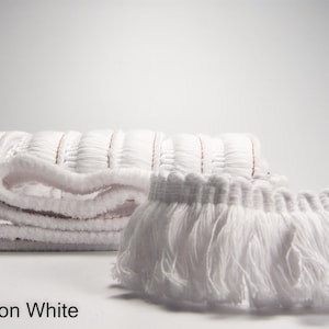 May include: White cotton fringe trim with a folded piece of the same trim in the background. The text "Cotton White" is visible at the bottom of the image.