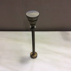 Puede incluir: Una lámpara de metal alta y delgada con una pantalla en forma de cono. La lámpara es de color gris oscuro con una base dorada.