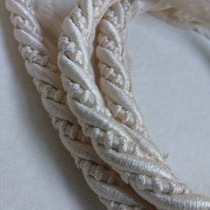 May include: Close-up of a white, braided rope cord. The cord is twisted and looped, showing the intricate details of the braid.