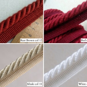 May include: Close-up of four samples of decorative rope trim in various colors. The colors include rust brown, red, khaki, and white. Each trim has a twisted rope design with a woven edge. The text "Rust Brown col 12", "Red col 15", "Khaki col 18", and "White col 20" are visible.