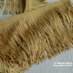 Op de afbeelding: Een close-up van een gouden franje trim. De franje is gemaakt van dunne, strak geweven draden. De trim is ongeveer 2,5 cm breed. De tekst "Yellow Gold col 6" is zichtbaar in de rechterbenedenhoek van de afbeelding.