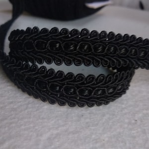 Puede incluir: Borde trenzado negro con un patrón decorativo de bucles y espirales. El borde tiene aproximadamente 2,5 cm de ancho.