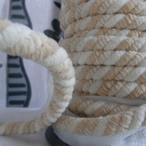 May include: A spool of white and beige braided cord with a fuzzy texture. The cord is twisted and has a rope-like appearance.