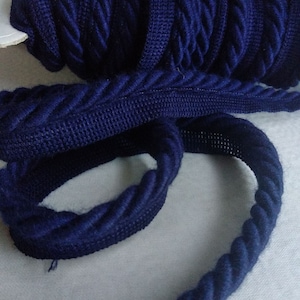 May include: A close-up of a navy blue braided trim. The trim is made of a soft, textured fabric and has a rope-like appearance.