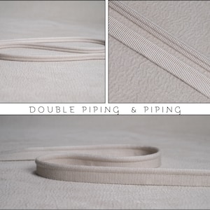 May include: A beige fabric trim featuring double piping and single piping, with a textured surface. The text DOUBLE PIPING & PIPING is displayed in the center. The trim consists of a corded edge attached to a flat fabric strip for sewing.