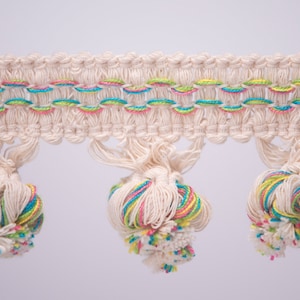 May include: White cotton trim with colourful pom-poms. The trim has a woven design with green, blue, and pink threads.