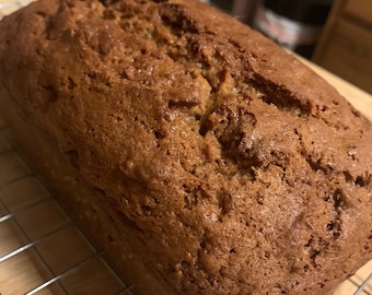 May include: A golden brown loaf of banana bread, freshly baked and cooling on a wire rack.