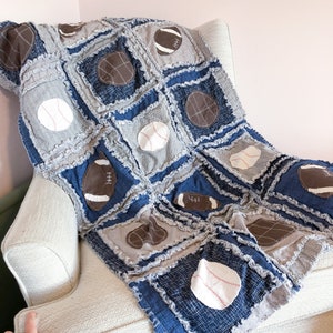 May include: A blue and gray patchwork quilt with a variety of sports-themed appliques, including baseballs, footballs, and basketballs.