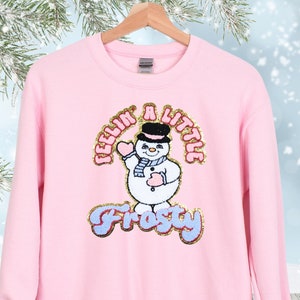 May include: Pink sweatshirt with a snowman graphic and the text "Feelin' a Little Frosty".