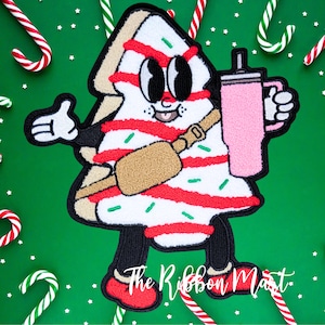 May include: A red and white striped Christmas tree character with green sprinkles, wearing a brown crossbody bag and holding a pink cup with a straw. The tree is smiling and has big eyes. The text "The Ribbon Mart" is visible at the bottom of the image.