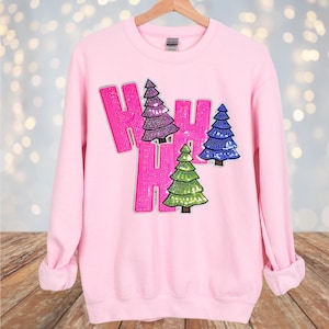 May include: Pink sweatshirt with a sparkly pink "Ho Ho Ho" design featuring three sequined Christmas trees in green, blue, and purple.
