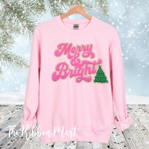 May include: Pink sweatshirt with a fuzzy pink and brown "Merry & Bright" design with a green Christmas tree.