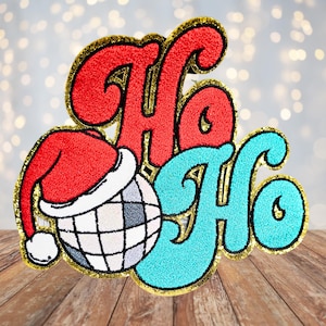 May include: A festive Christmas ornament featuring the words "Ho Ho" in a retro style, with a red Santa hat and a disco ball.