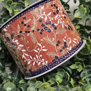 May include: A roll of decorative ribbon featuring a rust-colored background with a floral pattern in gold, white, and navy blue. The ribbon's edges are trimmed with a navy blue border, suitable for crafts and gift wrapping.