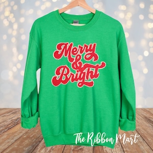 May include: Green Christmas sweatshirt with red and gold glitter lettering that says "Merry & Bright".