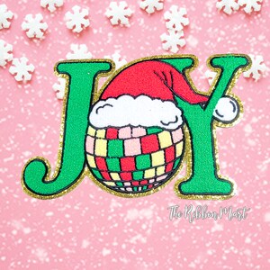 May include: Green felt "JOY" letters with gold glitter trim. The "O" is a red and white Santa hat with a green, red, and yellow striped ornament inside.