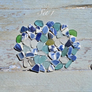 Pode incluir: Uma coleção de peças de vidro do mar sortidas em tons de azul, branco e verde, incluindo vários fragmentos com desenhos estampados em azul e branco. As peças estão dispostas em grupo, com o texto Set 1 visível acima da coleção.