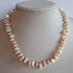 May include: A white pearl necklace with gold beads. The necklace is on a white mannequin.
