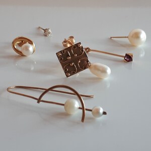May include: A set of four gold earrings with pearl accents. Two earrings feature a single pearl, one earring has a pearl dangling from a square charm, and the last earring has a pearl dangling from a curved wire.