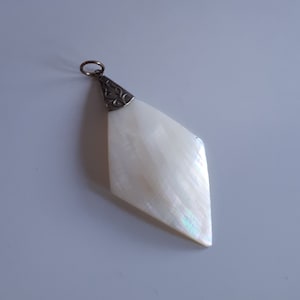 Puede incluir: Un colgante blanco iridiscente en forma de diamante con una anilla de filigrana plateada.