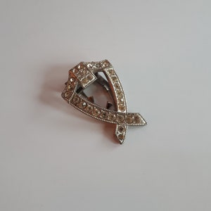 May include: A silver-toned brooch with a geometric design, featuring a cluster of clear rhinestones.