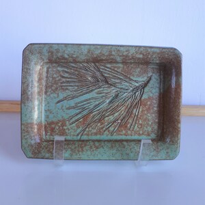 May include: A rectangular ceramic tray with a green glaze and brown accents. The tray features a raised design of a pine branch.