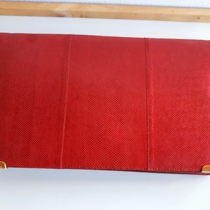 May include: A red leather clutch with gold hardware. The clutch has a textured surface and a rectangular shape.