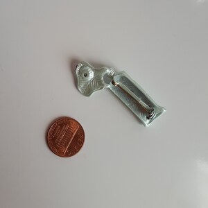 May include: A light green metal pin with a leaf design and a pin back. The pin is about the size of a US penny.