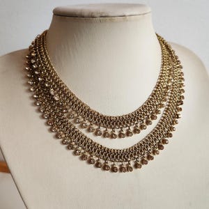 May include: A gold-tone layered necklace with a chain design and dangling crystal accents.