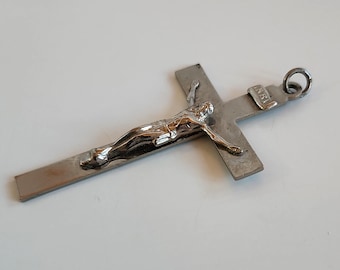 Puede incluir: Colgante de crucifijo plateado con una detallada representación de Jesucristo. La cruz tiene forma rectangular con un lazo para colgar. La figura de Cristo es de un color plateado contrastante. La inscripción 'INRI' es visible.