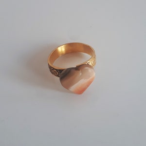 May include: A gold ring with a heart-shaped stone. The stone is a mix of brown, pink, and white.