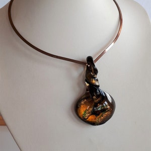 May include: A copper choker necklace with a twisted glass pendant. The pendant is a dark brown colour with swirls of gold and green.