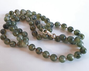 Puede incluir: Un collar de cuentas de jade verde con un cierre de plata. Las cuentas son redondas y tienen un color verde moteado.