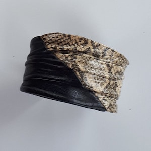 Puede incluir: Un brazalete de cuero negro y marrón con un patrón de piel de serpiente.