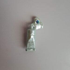 May include: A silver paint tube with a blue and green jewel on the cap.